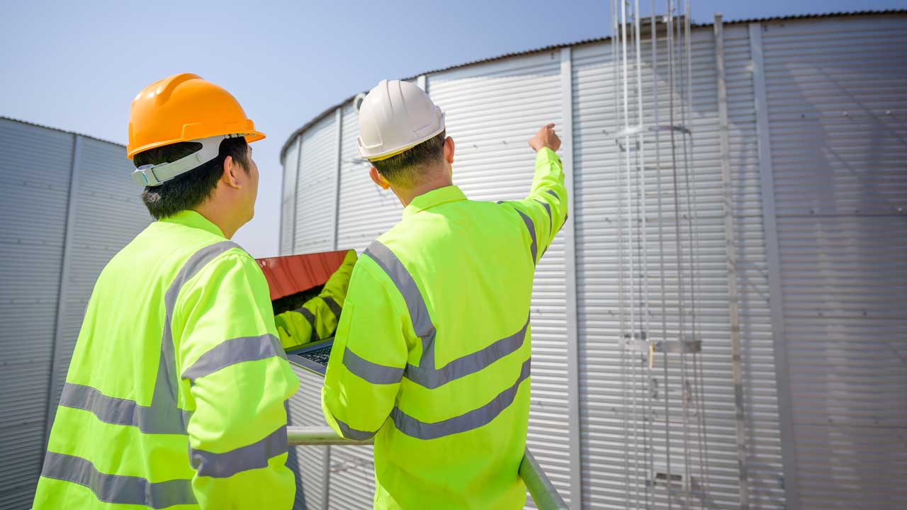 two men in high visibility jackets facing away from the camera inspecting water industry equipment 
